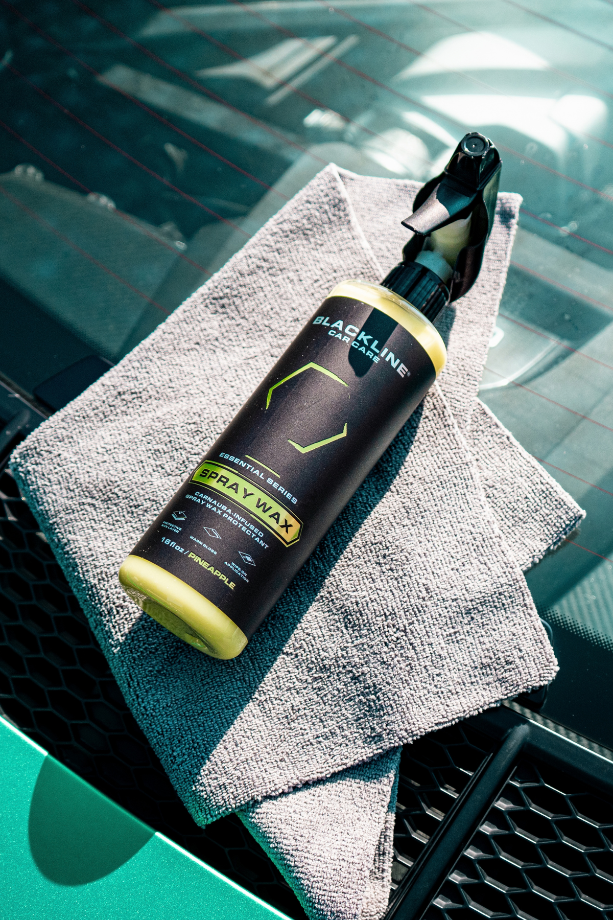 Hand spreading Blackline Spray Wax across a dark vehicle hood for paint protection.
