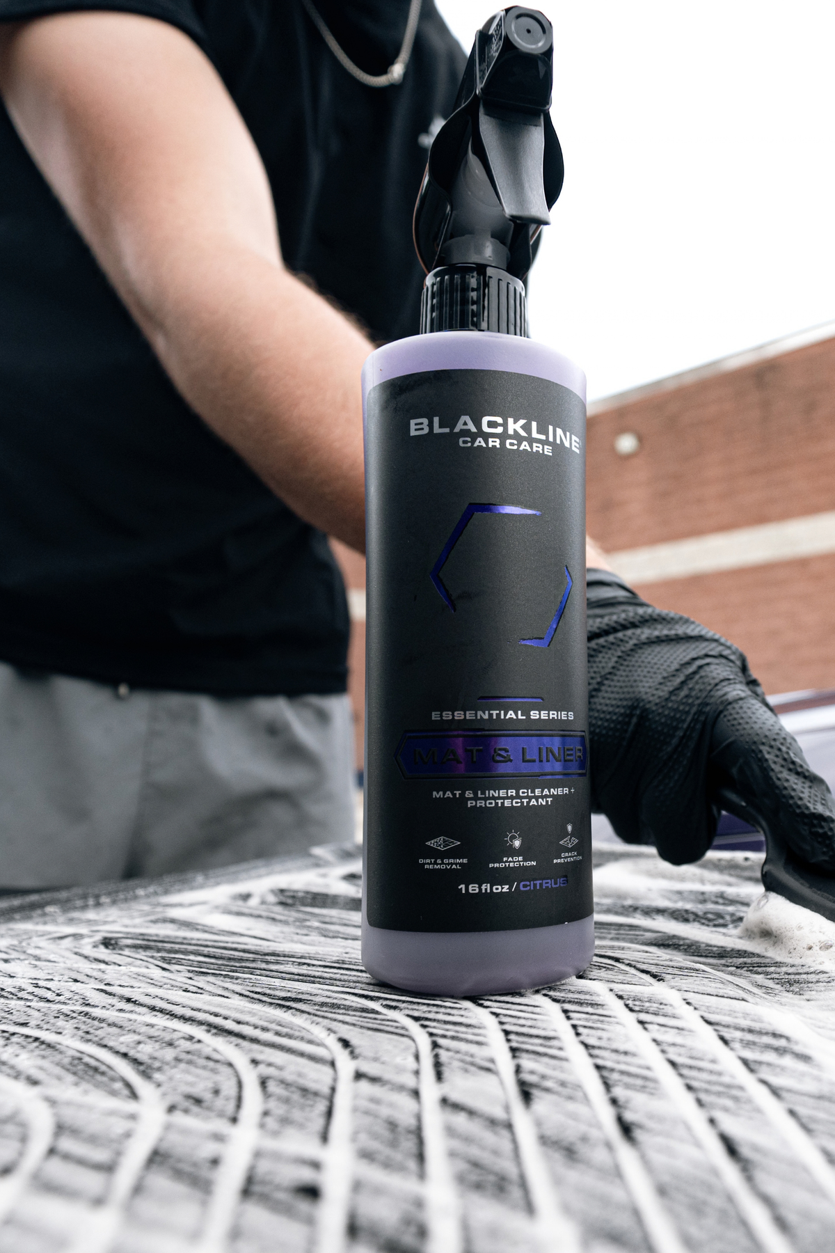 Hand scrubbing car floor mat with Blackline Mat and Liner cleaner using a brush.