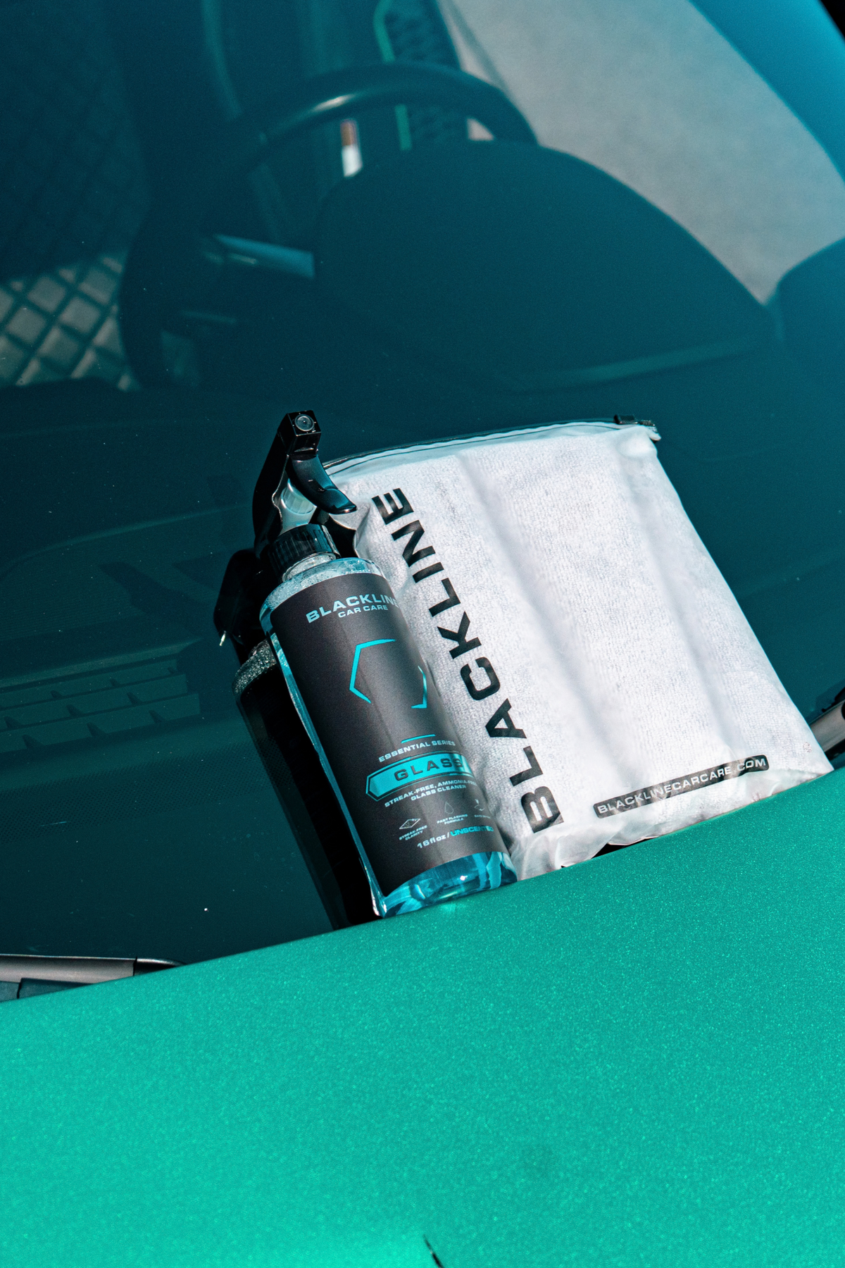 Hand spraying Blackline Glass cleaner onto car windshield for a streak-free finish.