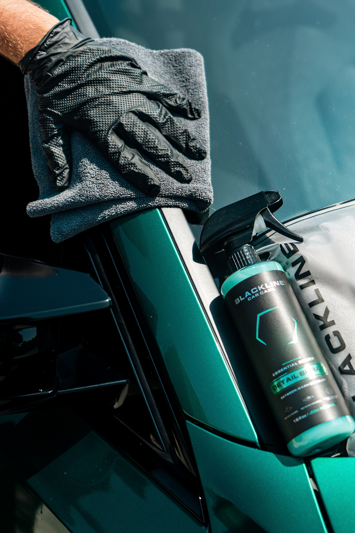 Hand using microfiber cloth with Blackline Detail Spray to buff black car paintwork.