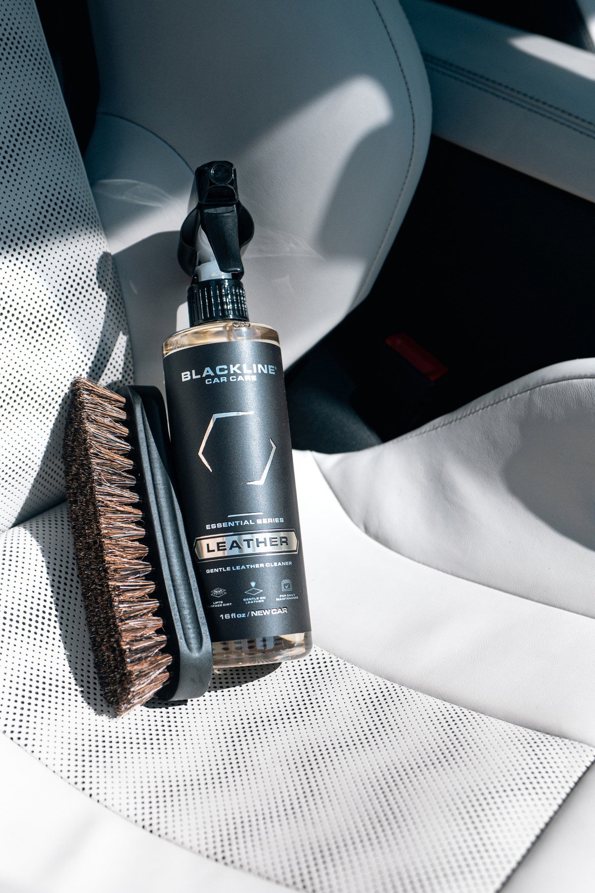 Hand using Blackline Leather cleaner on a luxury car door panel and stitching.