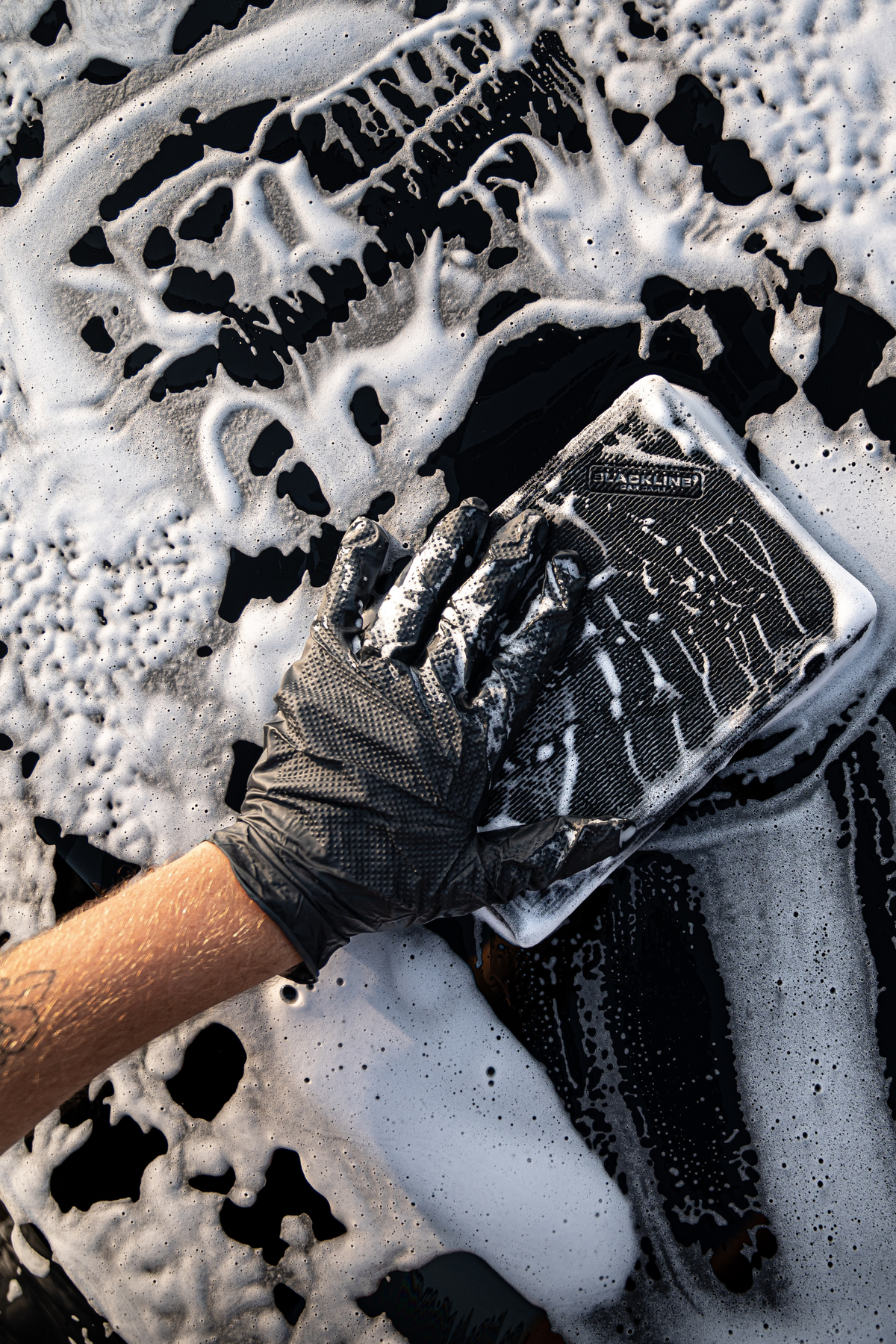 Blackline Clay Mitt decontaminating a dark-colored vehicle's paint during detailing.