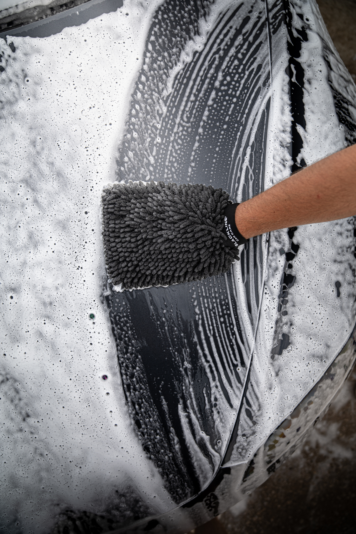 Blackline Chenille Wash Mitt resting beside a foam-filled wash bucket on a driveway.
