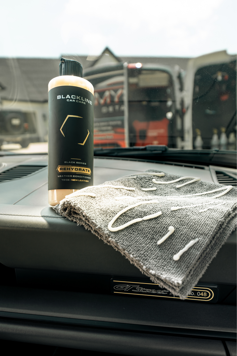 Hand applying Blackline Rehydrate Leather Conditioner to a vehicle's leather seat.