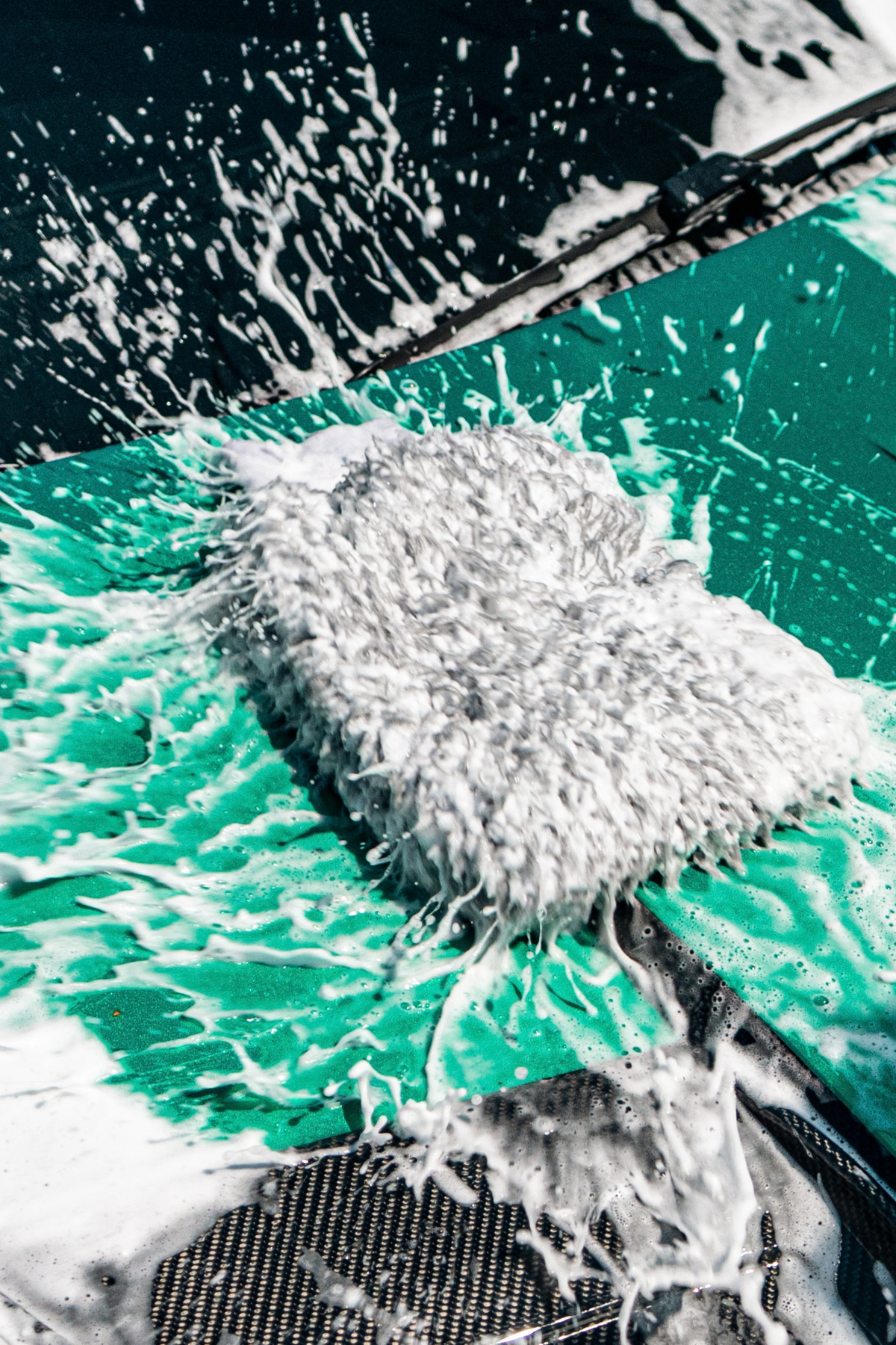 Hand with wash mitt using Blackline Shampoo to safely clean a dark vehicle panel.