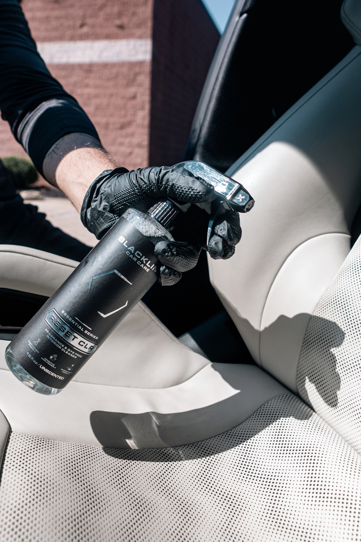 Hand spraying Blackline Reset CLR onto car upholstery for deep interior cleaning.