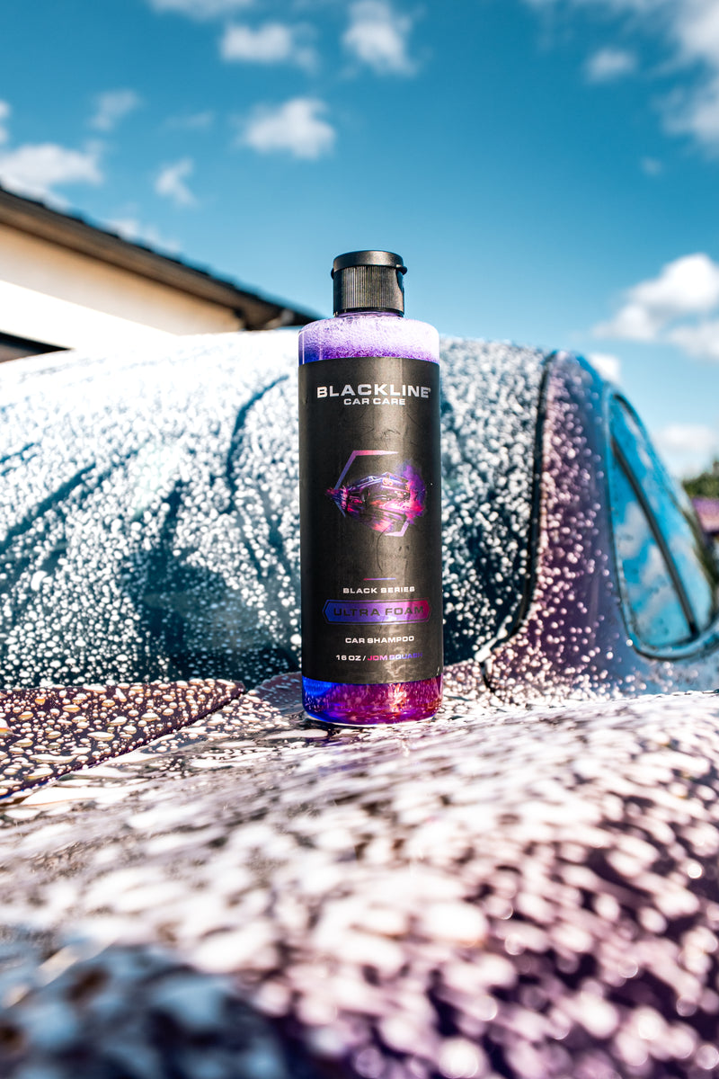 Blackline Ultra Foam JDM Squash 16oz bottle photographed outdoors on a foam-covered car hood with blue sky in the background.